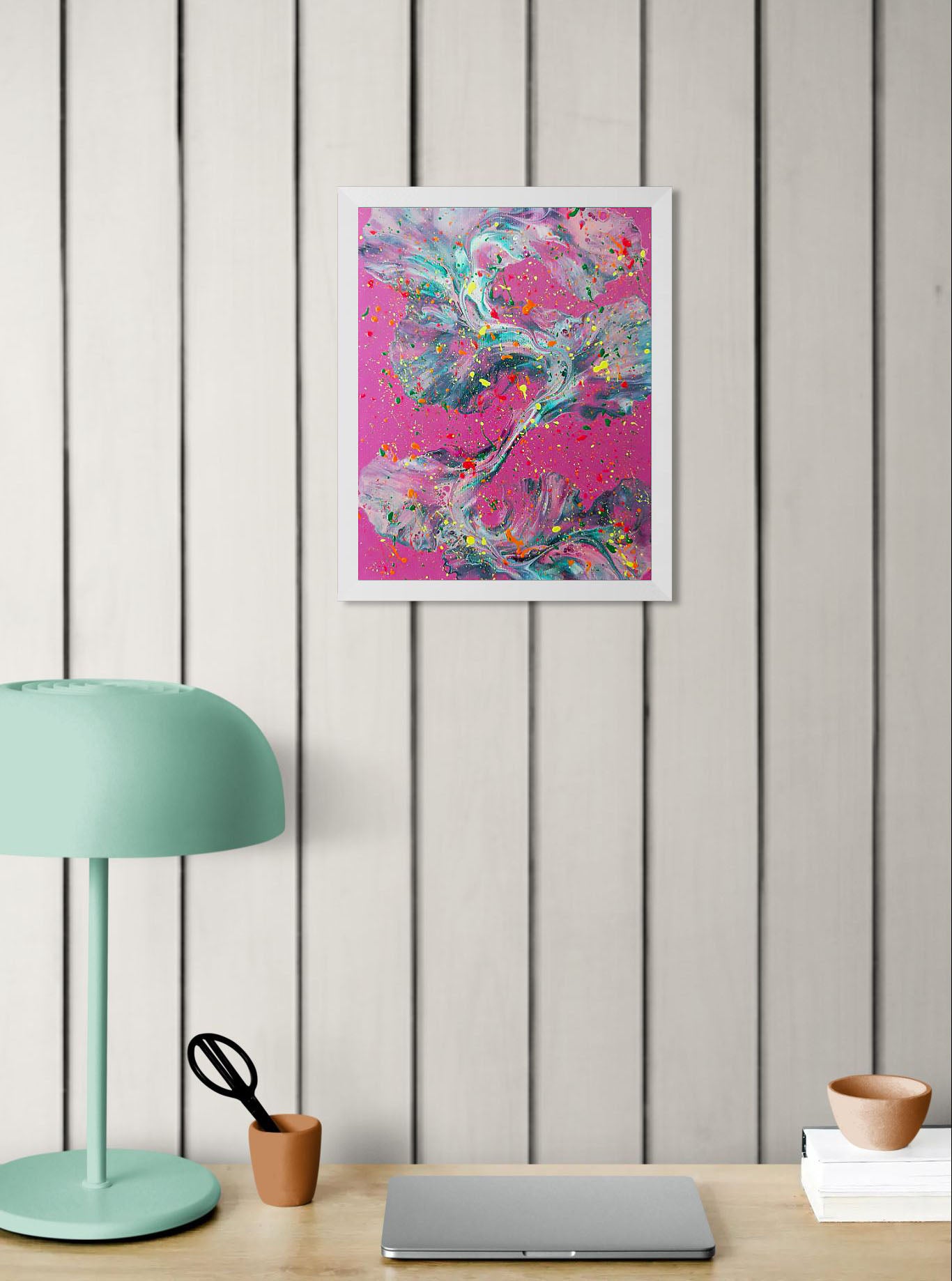 'That’s a Bold Choice' painting displayed on white paneled walls above a workspace with a mint-colored lamp, terracotta cup, and laptop, adding a bold pop of color to the room.