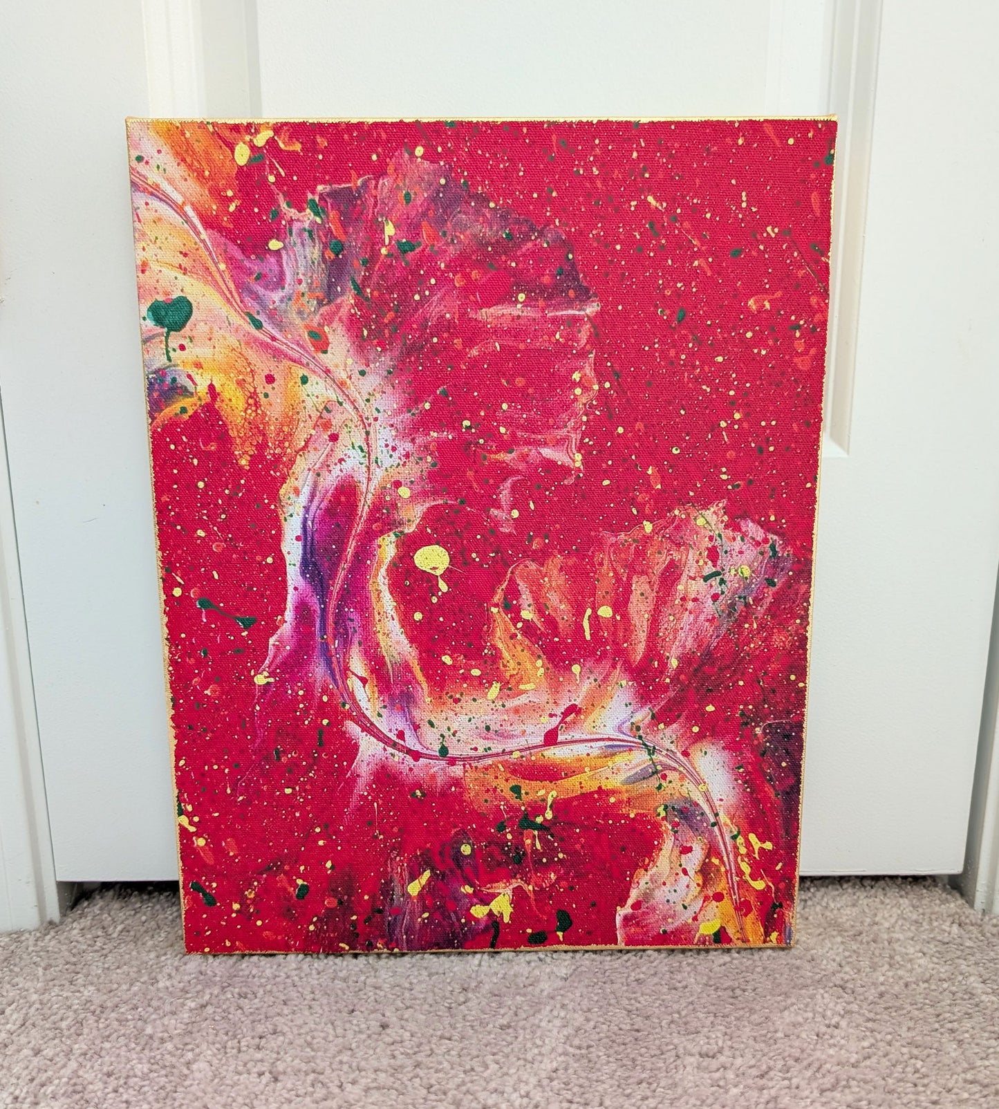 Front view of an abstract red fluid art canvas with swirling pink, purple, yellow, and white movement through the center, accented by splattered paint in various colors. The edges of the canvas are finished with gold leaf.