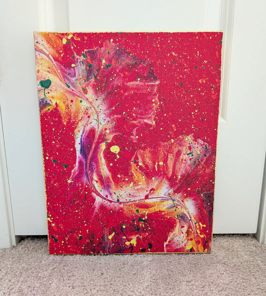 Front view of an abstract red fluid art canvas with swirling pink, purple, yellow, and white movement through the center, accented by splattered paint in various colors. The edges of the canvas are finished with gold leaf.
