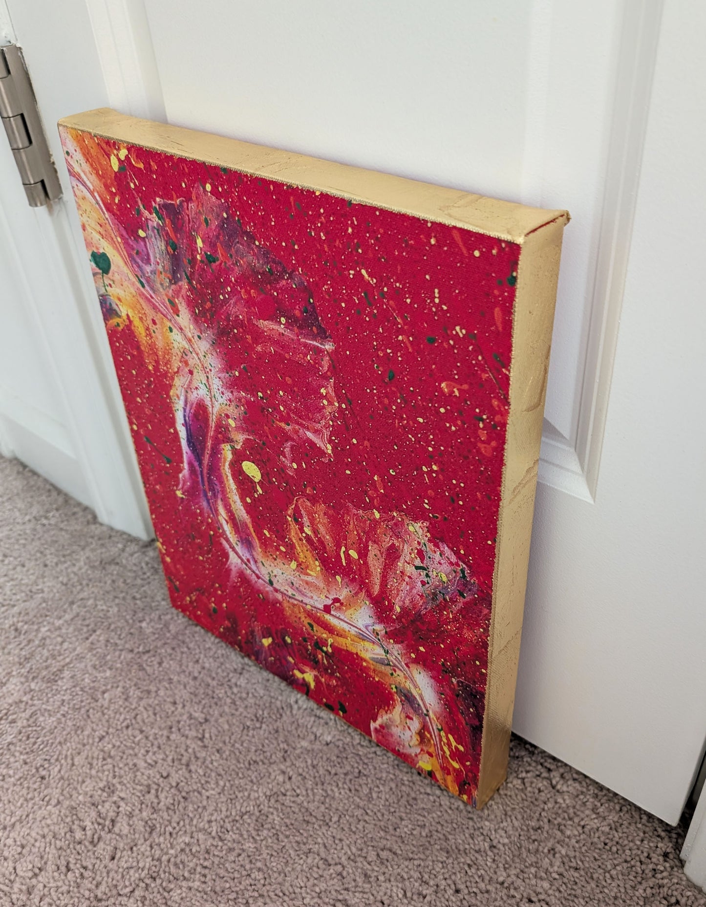 Another angled side view of the red fluid art canvas, focusing on the textured gold leaf edges and the swirling colorful details on the front surface.