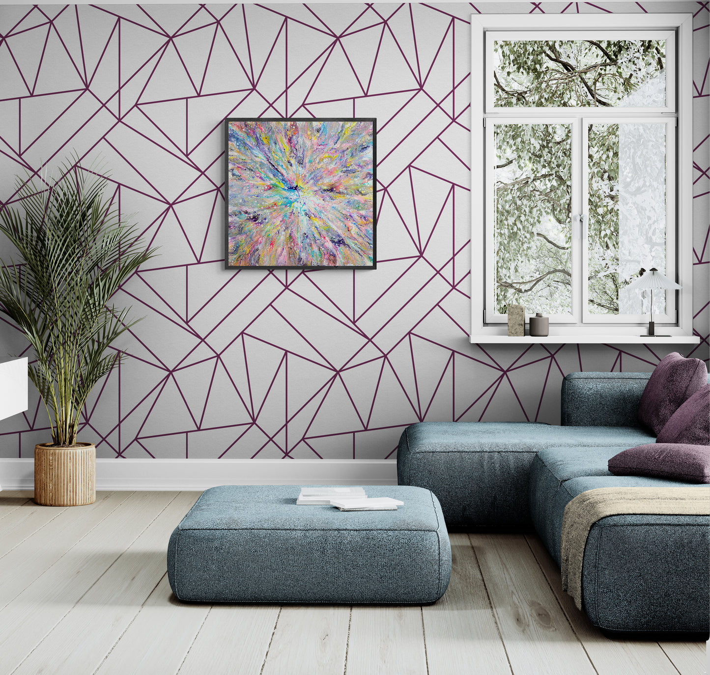 A vibrant abstract fluid painting with a burst of rainbow colors radiates from the center and hangs on a light gray wall with geometric purple linework. The room features a modern blue sectional with purple pillows, a low ottoman, and soft wood flooring. A window lets in natural light, and a leafy plant in a wicker pot adds a natural element to the bright, contemporary space.