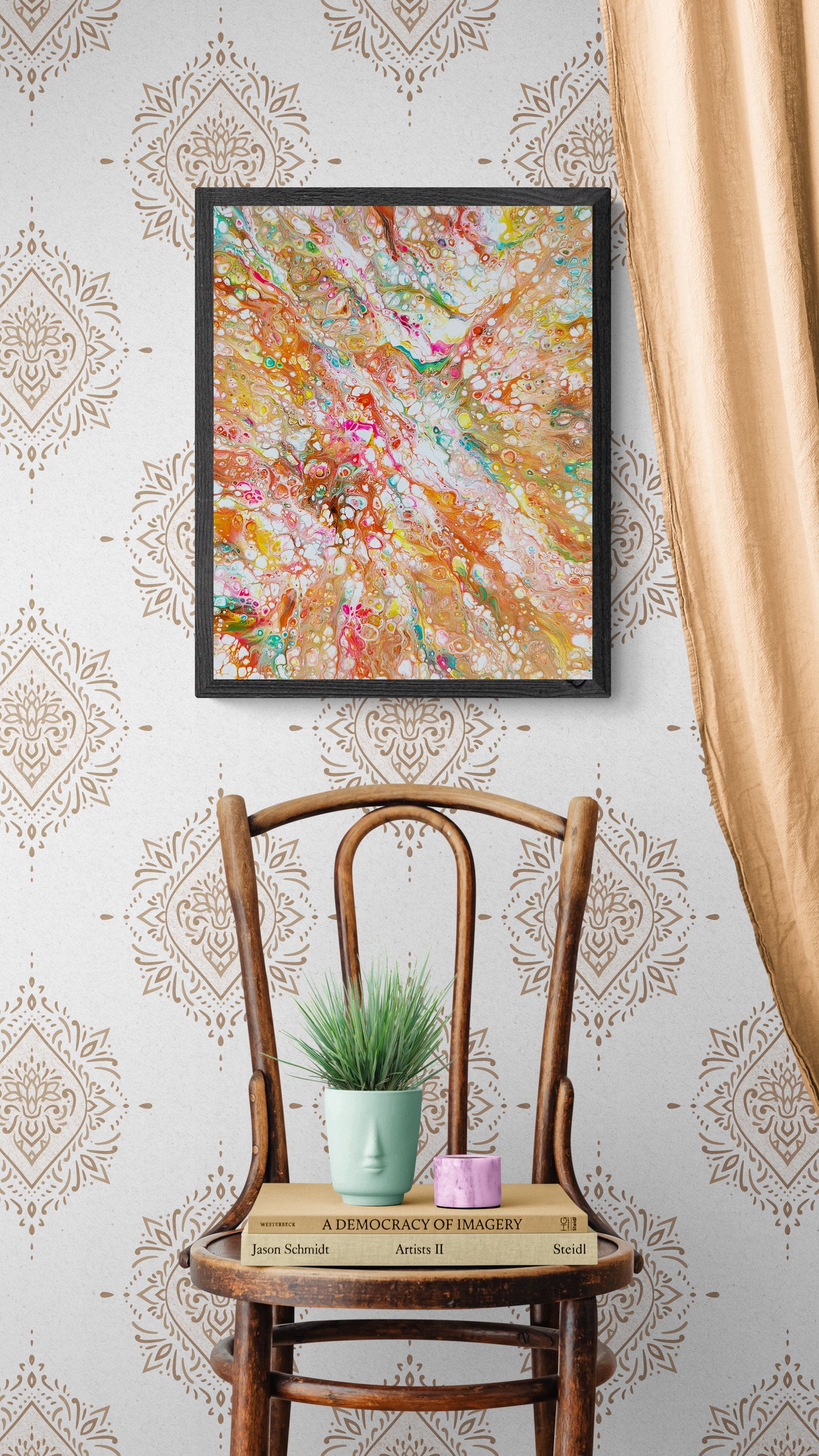 A framed abstract fluid painting in warm, vibrant tones of orange, pink, teal, and gold hangs on a patterned wall with tan damask wallpaper. Below it sits a vintage wooden chair holding a mint-green face-shaped vase with greenery, a candle, and stacked books. A golden curtain drapes into the frame from the right, adding a soft touch to the cozy and eclectic corner.