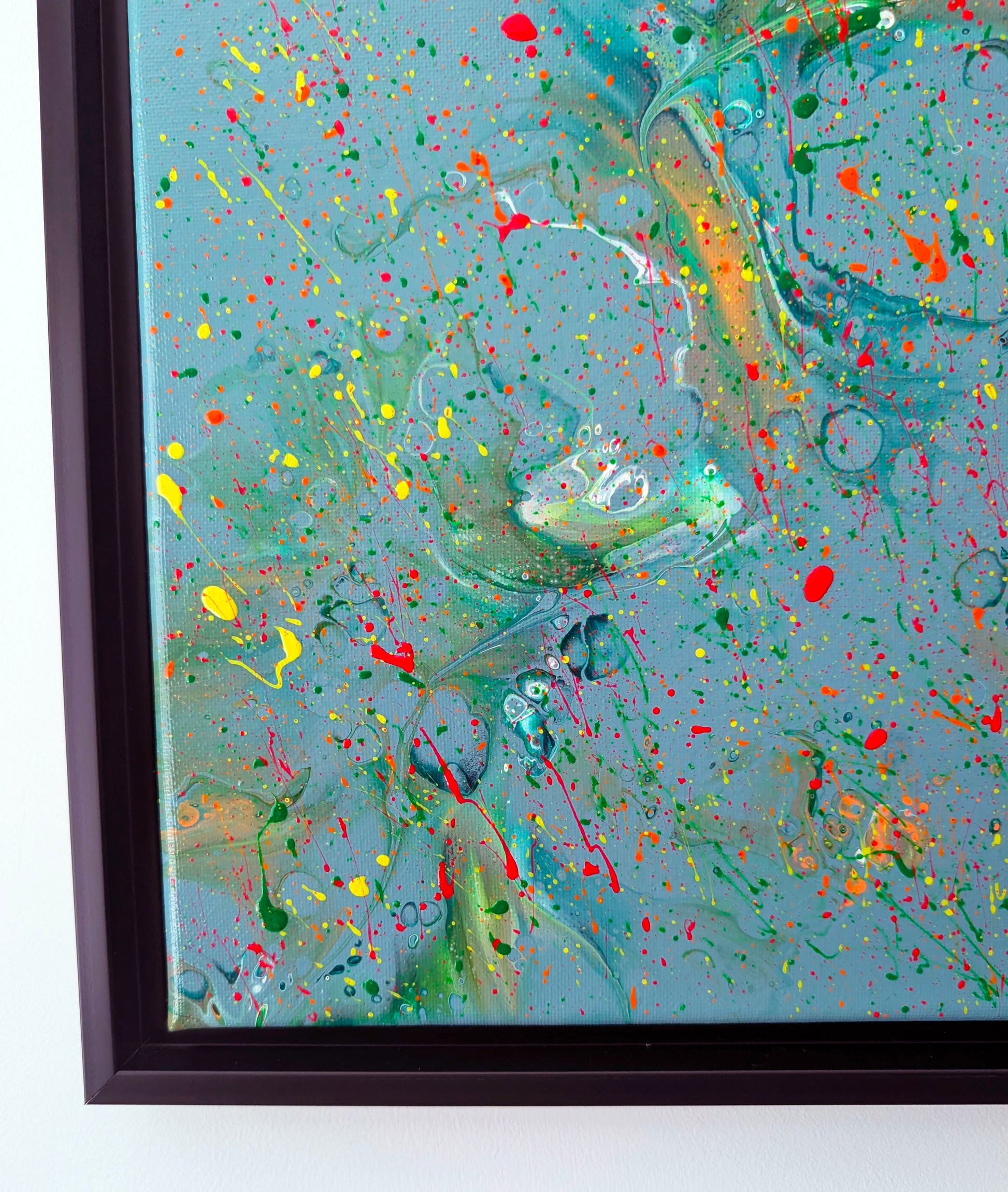Close-up of the bottom left corner of the painting, showing intricate layers of green, yellow, and red splatters over a teal blue base. Subtle marbling and cell-like patterns are visible, adding texture and detail.