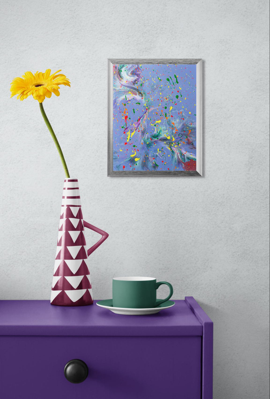 Mockup of the painting hanging on a light gray wall above a purple side table. A geometric maroon and white vase with a yellow flower and a green cup and saucer are placed on the table, adding a playful pop of color to the scene.