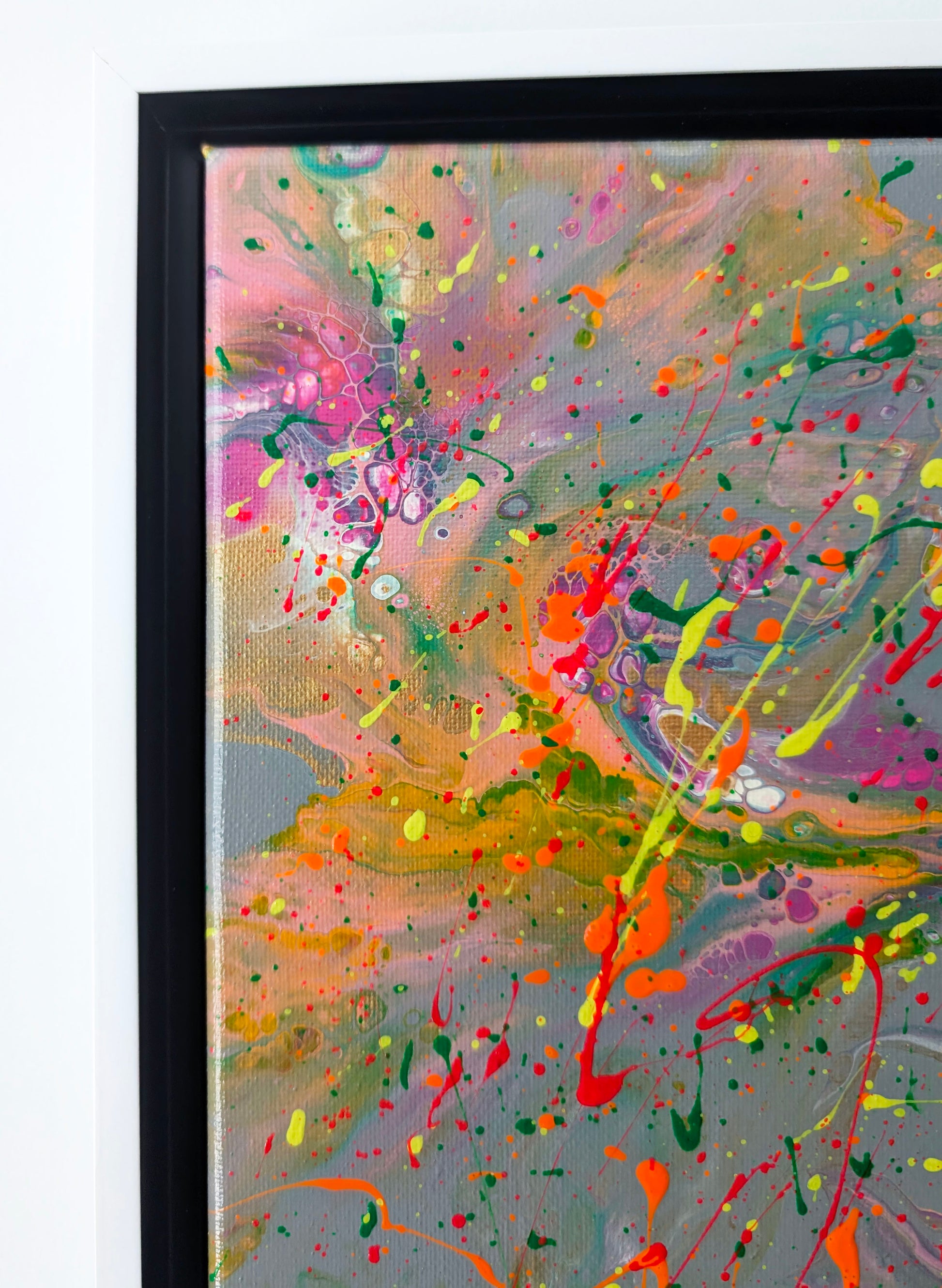 lose-up of the upper left corner of an abstract fluid painting, showing delicate pink, yellow, and orange swirls over gray with bright color splatters.