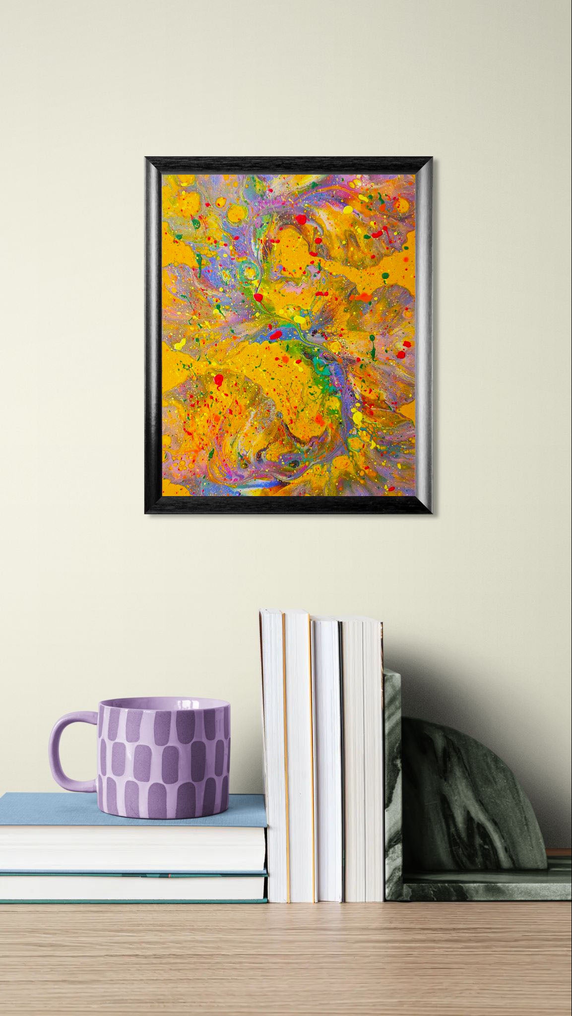 Mockup of the painting displayed on a neutral wall above a stack of books with a patterned lavender mug. The bright yellow and rainbow-hued painting provides a lively contrast to the soft-toned setting.