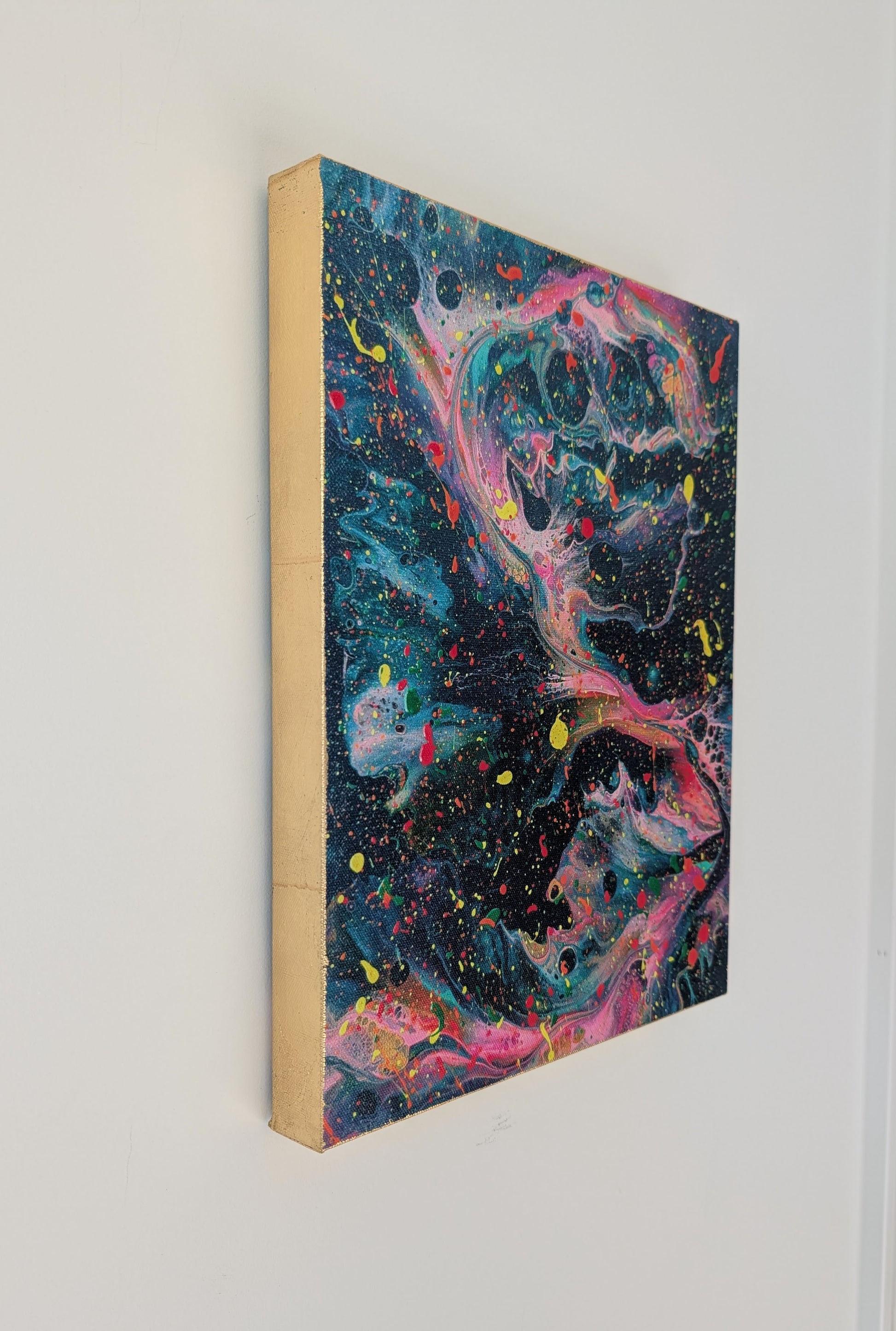 Side view of the dark abstract fluid art canvas hanging on a wall, focusing on the gold leaf edges and the vibrant swirling paint details.