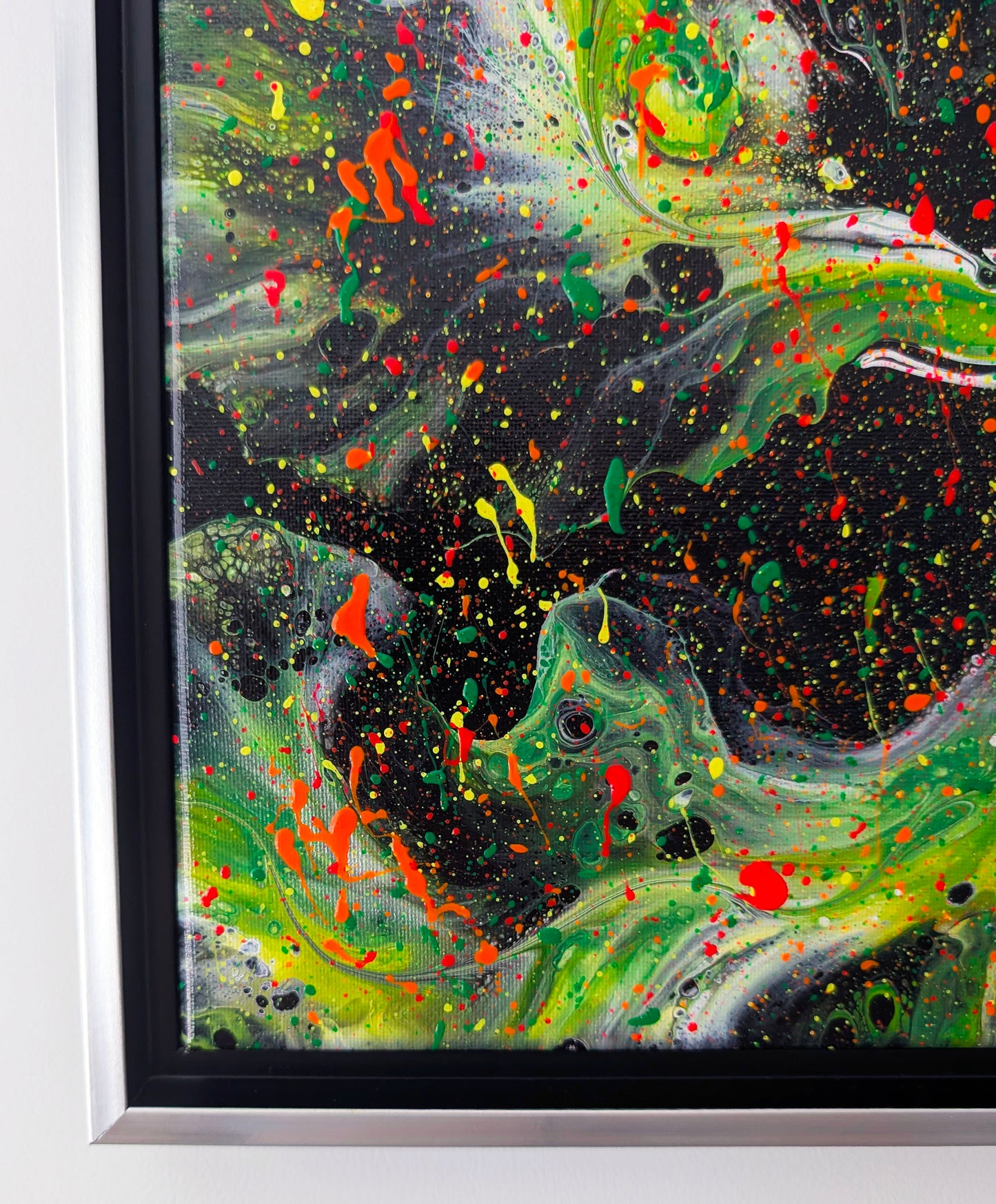 Close-up of the painting’s lower corner, showing a mix of green waves, black negative space, and bold orange-red drips. Fine splatters of yellow and green add depth