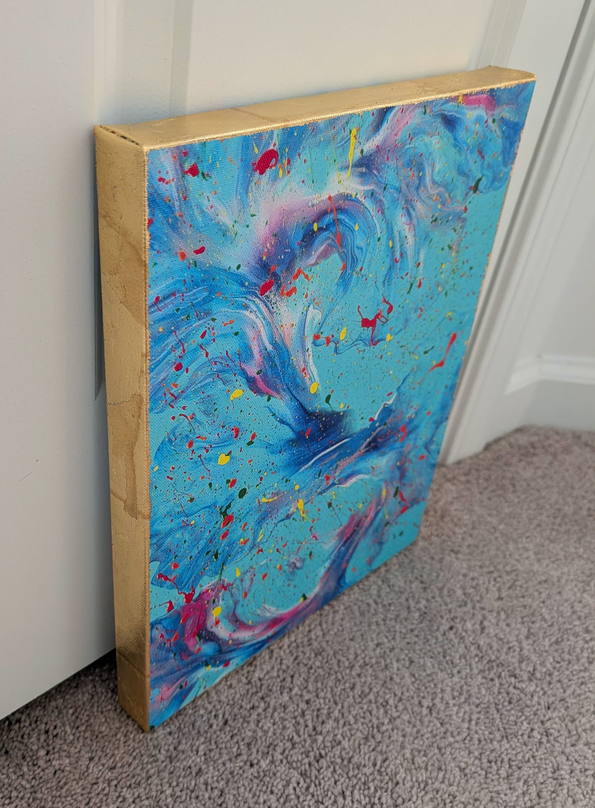 Side angle of the blue abstract fluid art canvas showing the hand-applied gold leaf covering the edges, contrasting with the vibrant swirling paint on the front