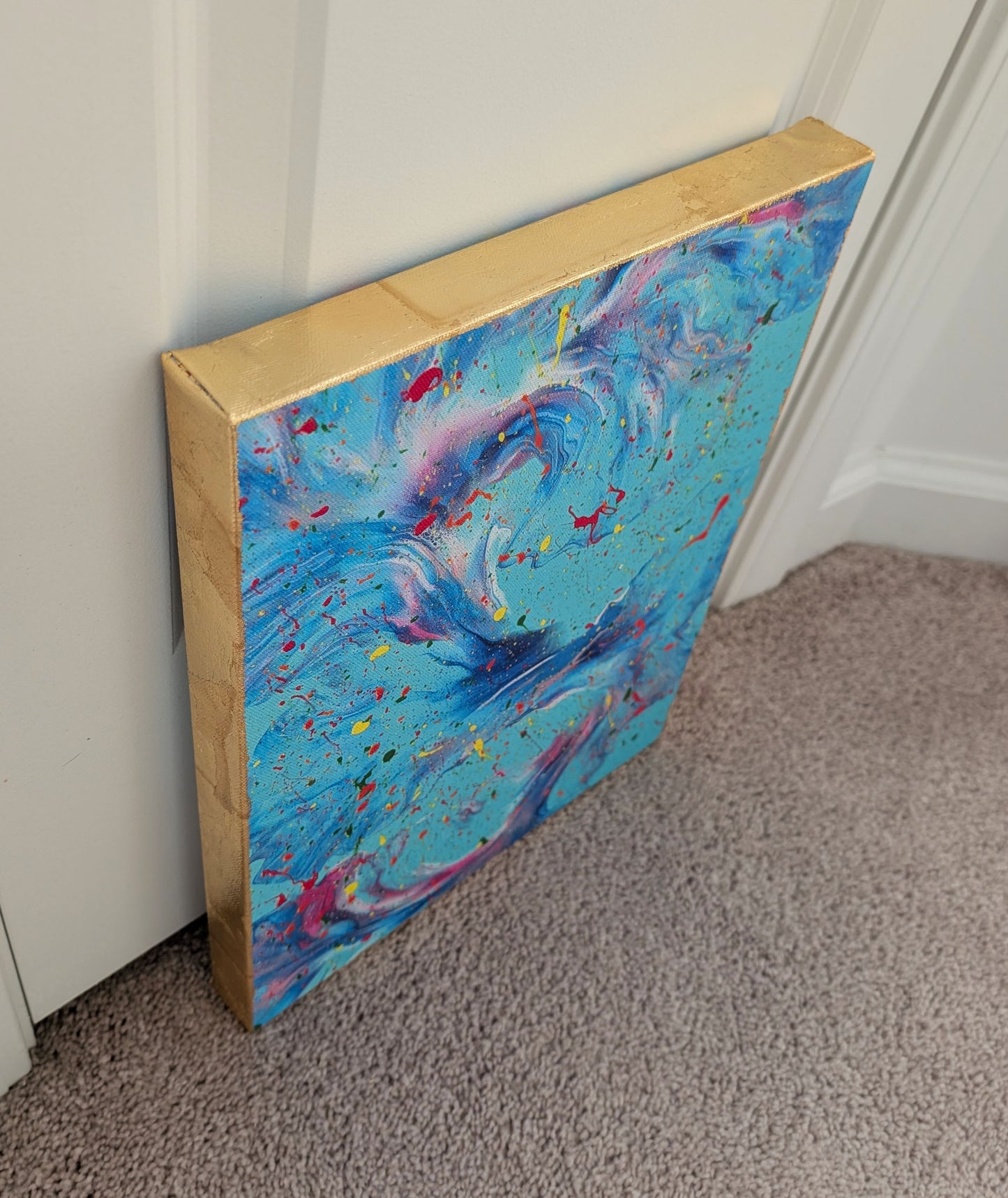 Angled side view of the blue fluid art canvas, highlighting the textured gold leaf edge and the bold paint splatters and marbled movement on the front.
