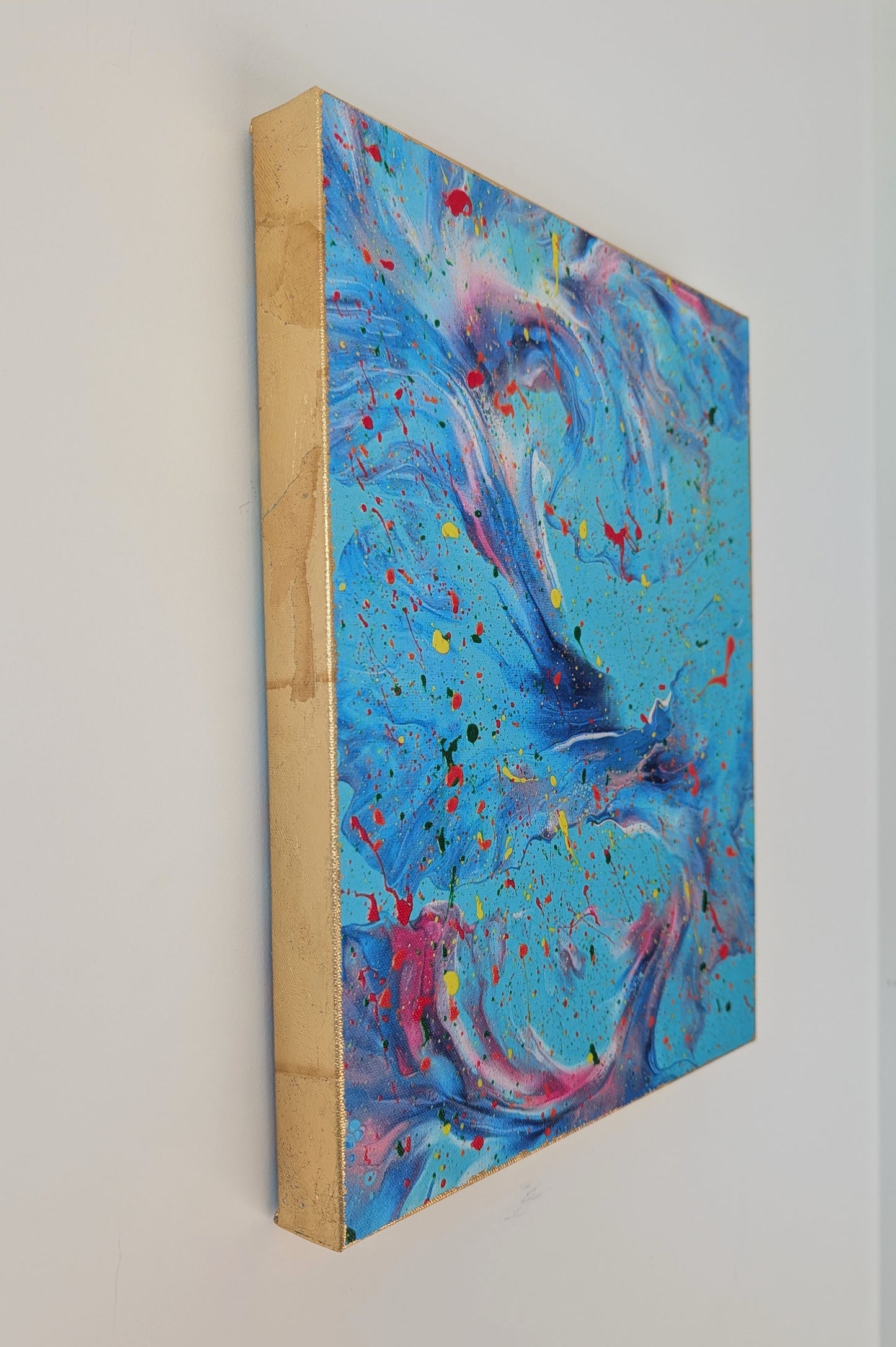 Side view of the blue fluid art canvas hanging on a wall, focusing on the metallic gold leaf edge and the vibrant layered paint details on the front.