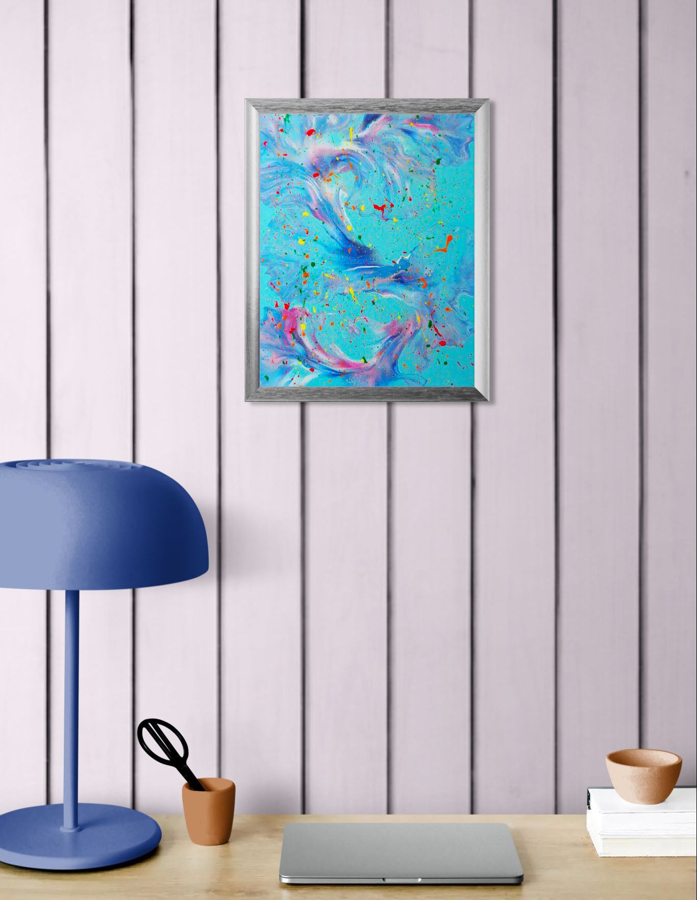 The painting shown in a workspace with pale lavender vertical wood paneling. It hangs above a desk with a periwinkle lamp and a laptop, offering a bright, creative focal point in the room.